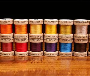 A wooden table with many different colored spools of thread.