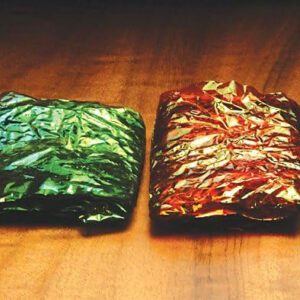 Two different colored foil wrapped food on a table.